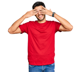 Young handsome man wearing casual red tshirt covering eyes with hands smiling cheerful and funny. blind concept.