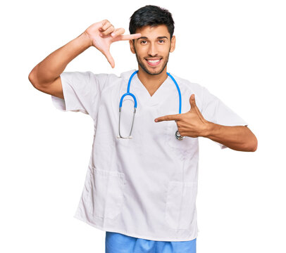 Young handsome man wearing doctor uniform and stethoscope smiling making frame with hands and fingers with happy face. creativity and photography concept.
