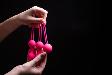Woman's hand holds pink Kegel balls / Ben Wa balls on a black isolated background. Vaginal balls in...