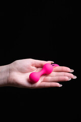 Woman's hand holds pink Kegel balls / Ben Wa balls on a black isolated background. Vaginal balls in a female hand. Sex toys Geisha balls. Place for text. Sex shop concept