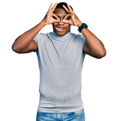 Naklejka premium Young black man wearing casual t shirt doing ok gesture like binoculars sticking tongue out, eyes looking through fingers. crazy expression.