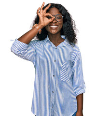 Beautiful african young woman wearing casual clothes and glasses doing ok gesture with hand smiling, eye looking through fingers with happy face.