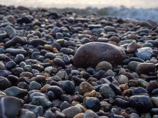 Pebbles on the seashore close-up. Rocky beach. Stones close-up with bokeh. Gray natural background. The concept of rest on the seashore. The Velvet season.   Waves and wet pebbles