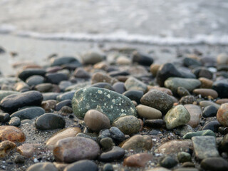 Pebbles on the seashore close-up. Rocky beach. Stones close-up with bokeh. Gray natural background. The concept of rest on the seashore. The Velvet season.   Waves and wet pebbles