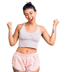 Young woman wearing sportswear very happy and excited doing winner gesture with arms raised, smiling and screaming for success. celebration concept.