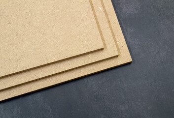 Three boards of raw mdf stacked on top of each other, on a dark background.