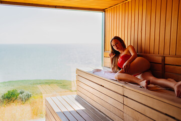 woman in a red swimsuit lies on a bench in the sauna with the panoramic window. 