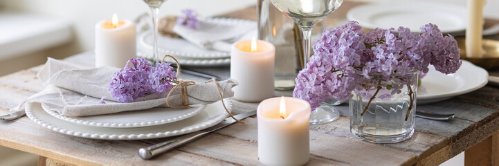 Beautiful table decor for a wedding dinner with a spring blooming lilac flowers. Celebration of a special event. Fancy white plates, and wineglasses. Countryside style. Banner