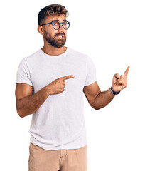 Young hispanic man wearing casual clothes and glasses pointing aside worried and nervous with both...