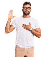 Young hispanic man wearing casual clothes and glasses swearing with hand on chest and open palm,...