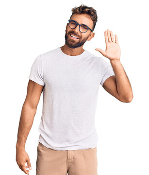 Young hispanic man wearing casual clothes and glasses waiving saying hello happy and smiling, friendly welcome gesture