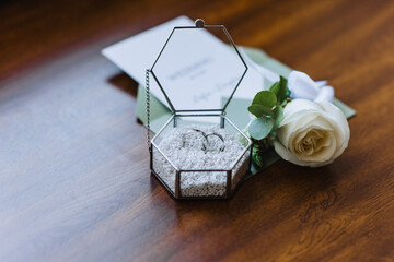 Wedding details and accessories close-up: a boutonniere, gold rings in a glass box, an envelope...
