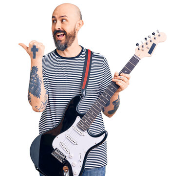 Young handsome man playing electric guitar pointing thumb up to the side smiling happy with open mouth