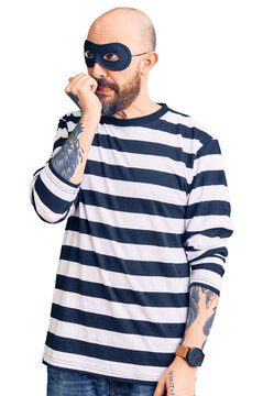 Young handsome man wearing burglar mask looking stressed and nervous with hands on mouth biting nails. anxiety problem.