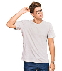 Handsome caucasian man wearing casual clothes and glasses confuse and wondering about question. uncertain with doubt, thinking with hand on head. pensive concept.