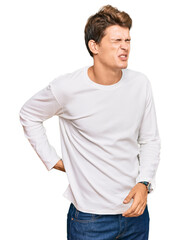 Fototapeta premium Handsome caucasian man wearing casual white sweater suffering of backache, touching back with hand, muscular pain