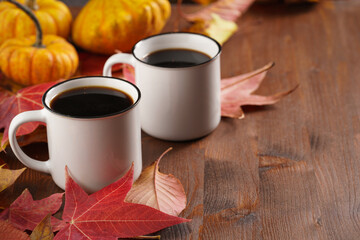 Naklejka na ściany i meble Two white cups with black coffee in a cozy autumn setting with red, yellow and orange leaves, hokkaido pumpkins, on wooden background