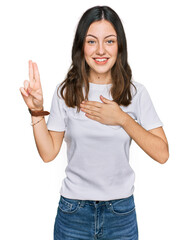 Young beautiful woman wearing casual white t shirt smiling swearing with hand on chest and fingers...