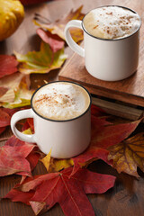 Two white cups with black coffee and white milk foam and cinnamon spice in a cozy autumn setting with red, yellow and orange leaves, hokkaido pumpkins, on wooden background