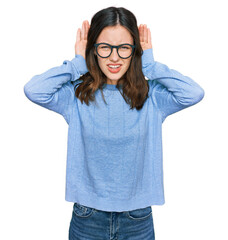 Young beautiful woman wearing casual clothes and glasses trying to hear both hands on ear gesture, curious for gossip. hearing problem, deaf