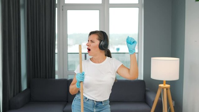 Woman cleans the house and have fun singing with a broom like a star
