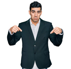 Handsome hispanic man wearing business clothes pointing down looking sad and upset, indicating direction with fingers, unhappy and depressed.