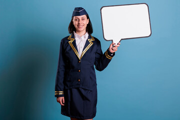 Smiling flight attendant holding white blank speech bubble, air hostess standing with communication...