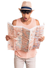 Young hispanic man wearing summer hat holding map scared and amazed with open mouth for surprise, disbelief face