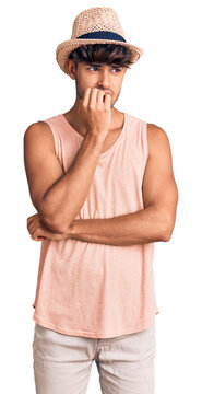 Young hispanic man wearing summer hat looking stressed and nervous with hands on mouth biting nails. anxiety problem.