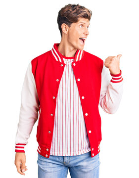 Young handsome man wearing baseball uniform smiling with happy face looking and pointing to the side with thumb up.