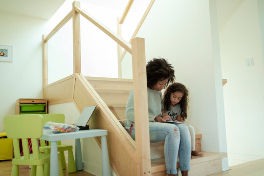 Mother and daughter using digital tablet on wooden stairs