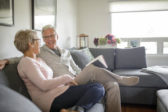 Smiling senior couple relaxing, reading book on living room sofa