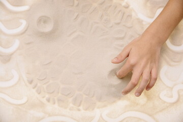 The child draws with fingers on the light table with quartz sand to develop motor skills