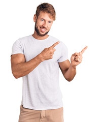 Young caucasian man wearing casual white tshirt smiling and looking at the camera pointing with two hands and fingers to the side.