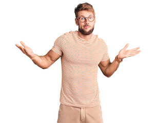 Young caucasian man wearing casual clothes and glasses clueless and confused expression with arms and hands raised. doubt concept.