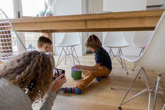 Mother with camera phone photographing sons playing with Easter eggs on hardwood floor