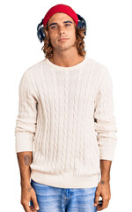 Young hispanic man listening to music using headphones relaxed with serious expression on face. simple and natural looking at the camera.