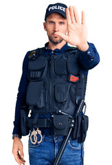 Young handsome man wearing police uniform doing stop sing with palm of the hand. warning expression...