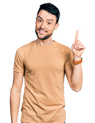 Naklejka premium Hispanic man with beard wearing casual t shirt pointing finger up with successful idea. exited and happy. number one.