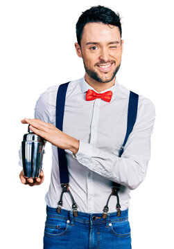 Hispanic man with beard preparing cocktail mixing drink with shaker winking looking at the camera with sexy expression, cheerful and happy face.