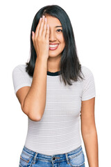 Beautiful asian young woman wearing casual white t shirt covering one eye with hand, confident smile on face and surprise emotion.