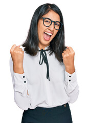 Beautiful asian young woman wearing business shirt and glasses screaming proud, celebrating victory and success very excited with raised arms