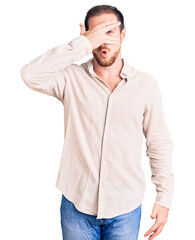 Young handsome caucasian man wearing casual clothes peeking in shock covering face and eyes with hand, looking through fingers with embarrassed expression.