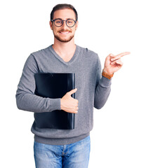 Young handsome caucasian man holding business folder smiling happy pointing with hand and finger to the side
