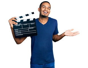 Young african american man holding video film clapboard celebrating achievement with happy smile...