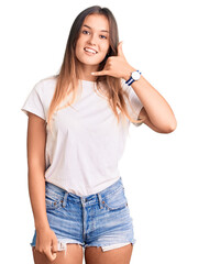 Beautiful caucasian woman wearing casual white tshirt smiling doing phone gesture with hand and fingers like talking on the telephone. communicating concepts.