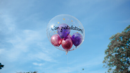 A Congratulations balloon with words "Congratulations!" floating in blue sky.