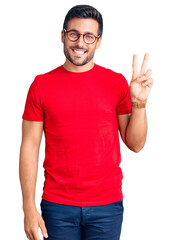 Fototapeta premium Young hispanic man wearing casual clothes and glasses smiling with happy face winking at the camera doing victory sign. number two.