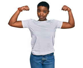 Young african american woman wearing casual white t shirt showing arms muscles smiling proud. fitness concept.