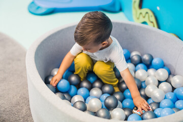 Fototapeta na wymiar Caucasian little boy sitting on the small balls and playing, kindergarten kids' concept. High quality photo